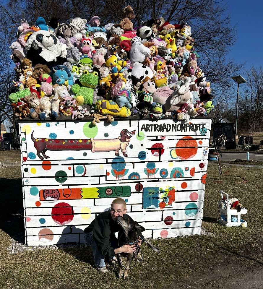 Callisto Martinez poses with their dog, a mutt with big ears, in front of a painted shed. 